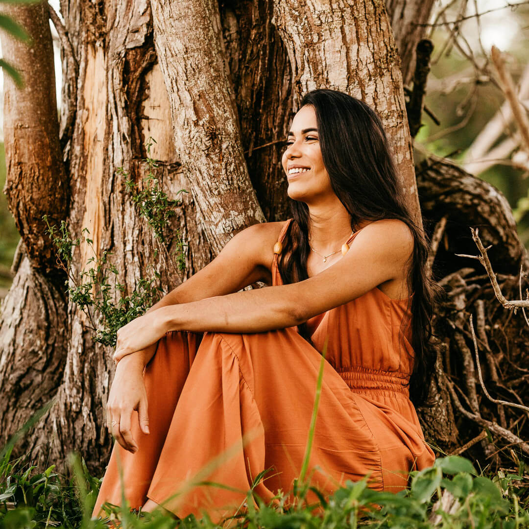 Femme brune assise contre un arbre avec une robe orange