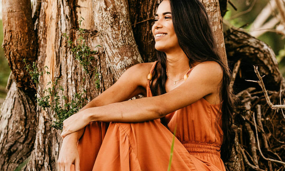 Femme brune assise contre un arbre avec une robe orange