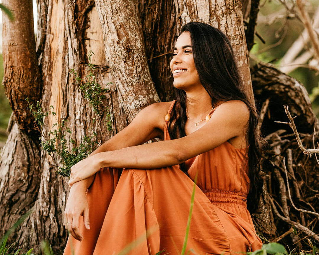 Femme brune assise contre un arbre avec une robe orange